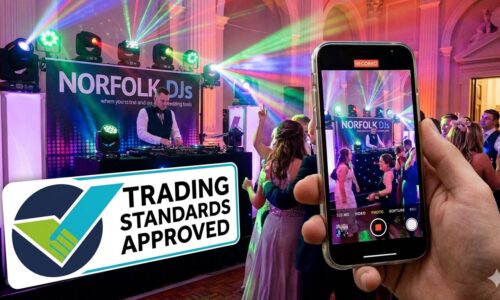 trading standards approved dj A hand holding a smartphone to film a wedding DJ performing behind a booth labeled "Norfolk DJs." Vibrant stage lights illuminate a dancing crowd, and a prominent "Trading Standards Approved" seal is overlaid in the foreground.